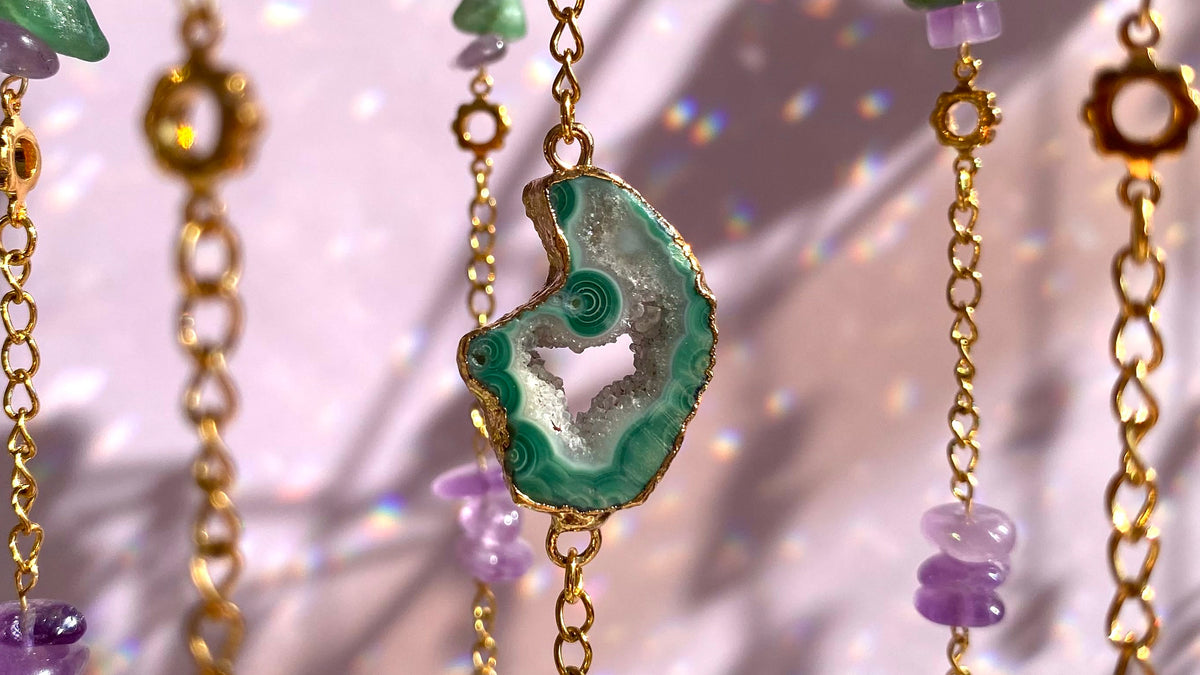 Drusa verde con borde dorado entre cadenas y amatistas, con destellos de luz